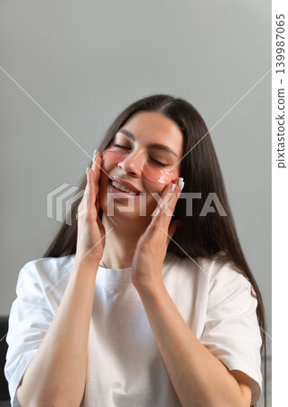 Vertical beauty portrait of young woman wearing hydrogel under-eye patches during skincare routine at home. Concept of self-care, healthy skin and modern facial treatment. 139987065