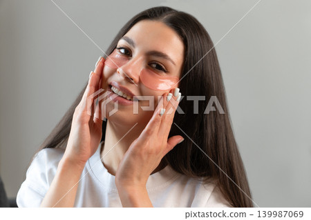 Young woman relaxing with hydrogel under-eye patches during daily skincare routine at home. Natural beauty portrait focused on self-care, healthy skin and modern cosmetic treatment. Young woman relaxing with hydrogel under-eye patches during daily skincare routine at home. Natural beauty portrait focused on self-care, healthy skin and modern cosmetic treatment. 139987069