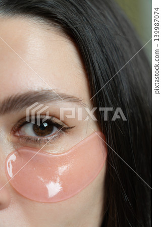 Crop sensual young female with dark hair in bathrobe putting collagen patches under eyes after shower standing against turquoise background Crop sensual young female with dark hair in bathrobe putting collagen patches under eyes after shower standing against turquoise background 139987074