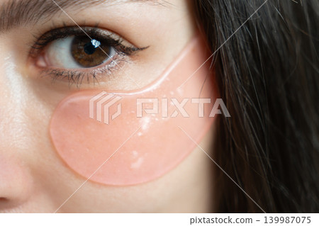 Crop sensual young female with dark hair in bathrobe putting collagen patches under eyes after shower standing against turquoise background Crop sensual young female with dark hair in bathrobe putting collagen patches under eyes after shower standing against turquoise background 139987075