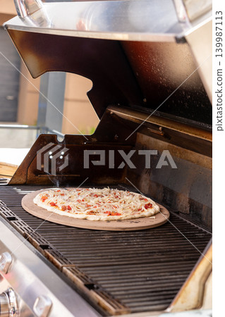 Vertical close-up of a freshly baked pizza on a pizza stone inside a gas grill. The image shows melted cheese, crispy crust, and detailed texture of the cooking process in an outdoor setting. Ideal Vertical close-up of a freshly baked pizza on a pizza stone inside a gas grill. The image shows melted cheese, crispy crust, and detailed texture of the cooking process in an outdoor setting. Ideal 139987113