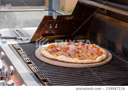 Close-up vertical shot of a freshly baked pizza placed on a pizza stone inside a gas grill. The image highlights melted cheese, crispy crust, and the cooking process in an outdoor setting. Perfect for Close-up vertical shot of a freshly baked pizza placed on a pizza stone inside a gas grill. The image highlights melted cheese, crispy crust, and the cooking process in an outdoor setting. Perfect for 139987116