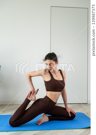 Vertical portrait of a fit young woman performing stretching and fitness exercises with resistance band at home. Female training indoors in sportswear during wellness and healthy lifestyle routine Vertical portrait of a fit young woman performing stretching and fitness exercises with resistance band at home. Female training indoors in sportswear during wellness and healthy lifestyle routine 139987373
