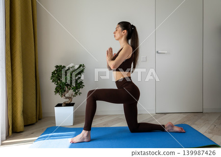 Young woman practicing stretching exercises with fitness resistance band at home. Female doing flexibility and mobility workout in cozy apartment interior. Healthy lifestyle, home fitness, wellness Young woman practicing stretching exercises with fitness resistance band at home. Female doing flexibility and mobility workout in cozy apartment interior. Healthy lifestyle, home fitness, wellness 139987426