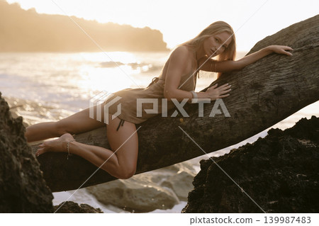 Young blonde woman posing on wooden log at beach Young blonde woman posing on wooden log at beach 139987483