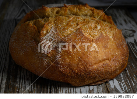 Freshly baked artisan bread resting on rustic wooden table after a warm oven finish Freshly baked artisan bread resting on rustic wooden table after a warm oven finish 139988097