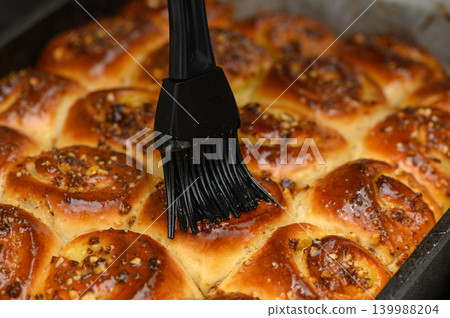 Warm cinnamon rolls being brushed with sweet glaze in a cozy kitchen setting during the morning hours Warm cinnamon rolls being brushed with sweet glaze in a cozy kitchen setting during the morning hours 139988204
