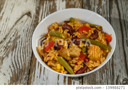 Flavorful rice dish with mixed vegetables and chicken on a rustic wooden table Flavorful rice dish with mixed vegetables and chicken on a rustic wooden table 139988271