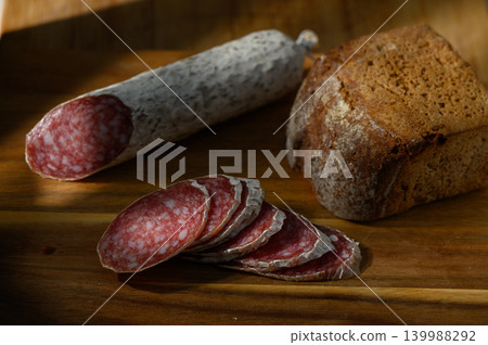 Delicious slices of salami beside rustic bread bathed in warm sunlight for the perfect snack moment Delicious slices of salami beside rustic bread bathed in warm sunlight for the perfect snack moment 139988292