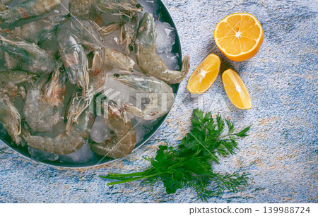 Fresh raw shrimp spread on ice with lemon and cilantro slices on a marble surface, ready to cook, no people 139988724