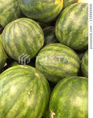 Fresh green watermelons stacked together in a sunlit market Fresh green watermelons stacked together in a sunlit market 139989400