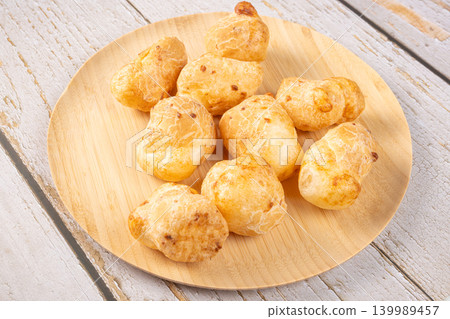 Cheese bread, a delicious Brazilian cheese bread, on a wooden plate on a rustic wooden surface, selective focus. Cheese bread, a delicious Brazilian cheese bread, on a wooden plate on a rustic wooden surface, selective focus. 139989457