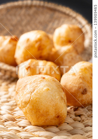 Cheese bread, a delicious Brazilian cheese bread, in a basket on a rustic woven straw surface, selective focus. Cheese bread, a delicious Brazilian cheese bread, in a basket on a rustic woven straw surface, selective focus. 139989465