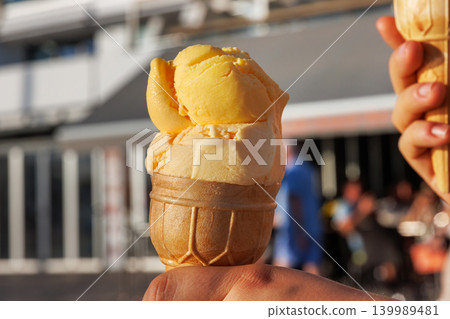 Close up of a hand holding an ice cream cone with a town building softly blurred in the background. Paphos, Cyprus 139989481