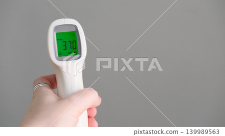 Hand holding infrared thermometer for temperature measure showing subfebrile 37 celsius degrees on green screen. Remote measurement of fever for children and public places, copy space. Flu season 139989563