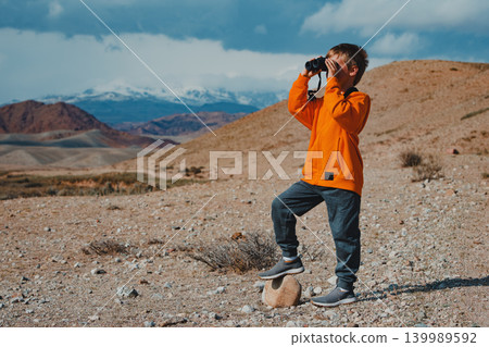 Boy tourist looking in binoculars in mountains Boy tourist looking in binoculars in mountains 139989592