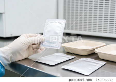 Scientist in sterile gloves holds sealed sample packaging over laboratory counter Scientist in sterile gloves holds sealed sample packaging over laboratory counter 139989948