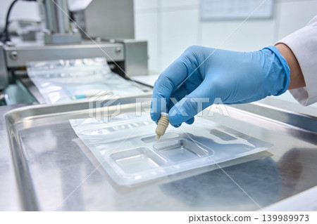 Scientist in blue gloves carefully places a small vial into a sterile medical packaging tray Scientist in blue gloves carefully places a small vial into a sterile medical packaging tray 139989973