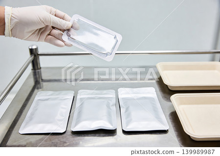Gloved hand holding sterile packaging over laboratory equipment and trays Gloved hand holding sterile packaging over laboratory equipment and trays 139989987