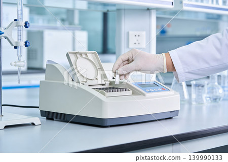 Scientist places sample vial into laboratory analyzer for testing Scientist places sample vial into laboratory analyzer for testing 139990133