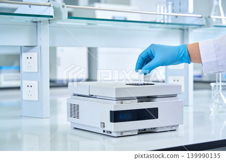 Scientist in blue gloves places sample vial into laboratory analysis equipment 139990135