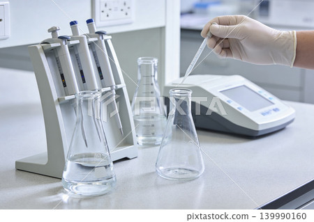 Scientist performing liquid handling with pipettes and flasks in a laboratory setting Scientist performing liquid handling with pipettes and flasks in a laboratory setting 139990160