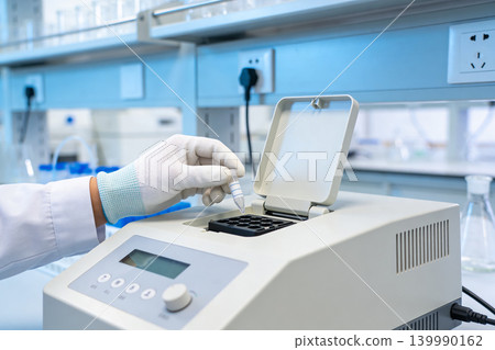 Scientist in lab coat and gloves places sample tube into thermal cycler machine Scientist in lab coat and gloves places sample tube into thermal cycler machine 139990162