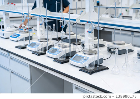 Modern laboratory equipment with digital scales and glassware arranged on a clean white bench 139990173