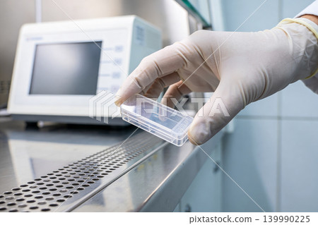 Scientist in sterile gloves holds a small plastic container for samples Scientist in sterile gloves holds a small plastic container for samples 139990225
