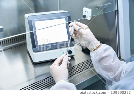 Scientist in sterile gloves and lab coat performs experiment with scientific equipment Scientist in sterile gloves and lab coat performs experiment with scientific equipment 139990252