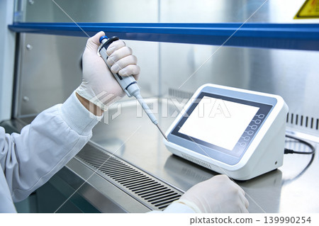 Scientist in sterile lab coat and gloves uses pipette with digital device 139990254