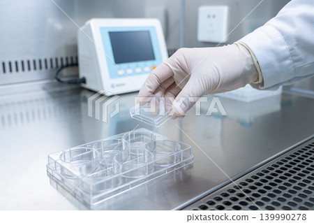Scientist in sterile gloves handles cell culture plate in a laboratory setting 139990278