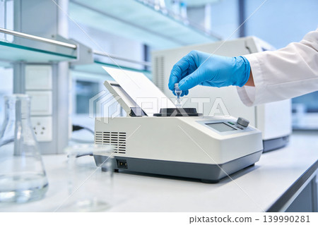 Scientist in blue gloves places vial into laboratory vortex mixer for sample preparation Scientist in blue gloves places vial into laboratory vortex mixer for sample preparation 139990281