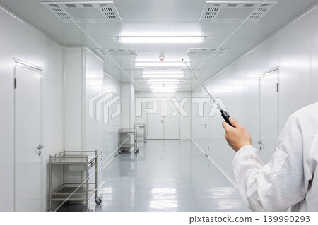 Scientist in cleanroom pointing with a probe down a sterile hallway with carts Scientist in cleanroom pointing with a probe down a sterile hallway with carts 139990293