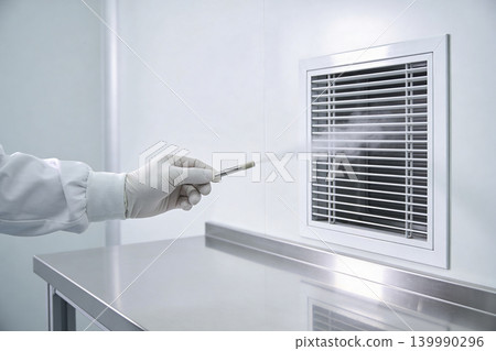 Scientist in sterile lab coat and gloves sprays mist near air vent for testing Scientist in sterile lab coat and gloves sprays mist near air vent for testing 139990296