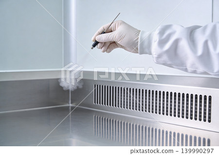Scientist in sterile lab coat and gloves sterilizing equipment with a mist sprayer Scientist in sterile lab coat and gloves sterilizing equipment with a mist sprayer 139990297