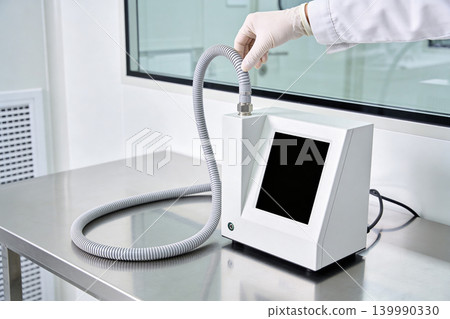 Scientist in lab coat connects flexible tube to modern scientific equipment Scientist in lab coat connects flexible tube to modern scientific equipment 139990330
