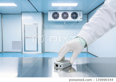 Scientist in sterile lab coat places small electronic device on shiny metal table 139990344