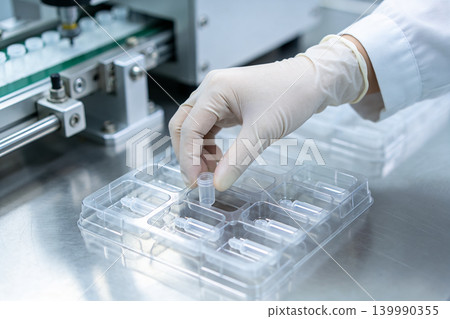 Scientist in sterile gloves places small vial into a laboratory tray for testing Scientist in sterile gloves places small vial into a laboratory tray for testing 139990355