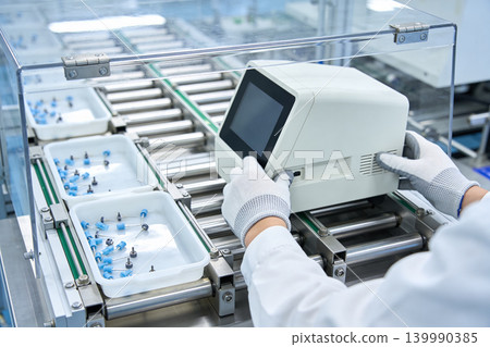 Automated medical device assembly line with technician in sterile gloves Automated medical device assembly line with technician in sterile gloves 139990385