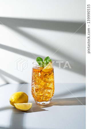 Iced tea with lemon and mint in a glass on a light background with shadows 139990535