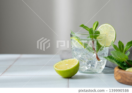 A fresh mojito with lime, mint and ice in glass. Citrus lemonade or cocktail on a table A fresh mojito with lime, mint and ice in glass. Citrus lemonade or cocktail on a table 139990586
