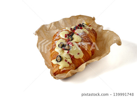 Crispy croissant with berries covered with white icing in parchment paper isolated on white background Crispy croissant with berries covered with white icing in parchment paper isolated on white background 139991748