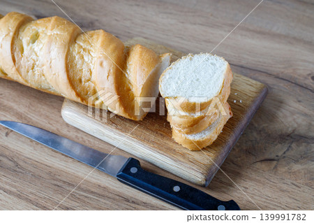 Fresh baguette cut with a knife. Slices of fresh bread on a wooden board. Rustic, handmade rye bread with a golden crust Fresh baguette cut with a knife. Slices of fresh bread on a wooden board. Rustic, handmade rye bread with a golden crust 139991782