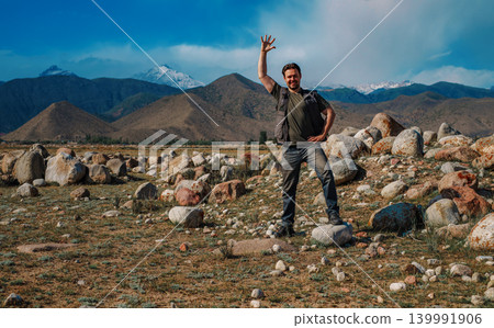 Young smiling man stands on mountain and waving his hand 139991906