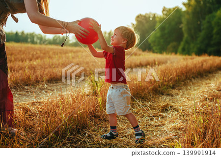 Young mother gives the ball to her two-year-old son in a field Young mother gives the ball to her two-year-old son in a field 139991914