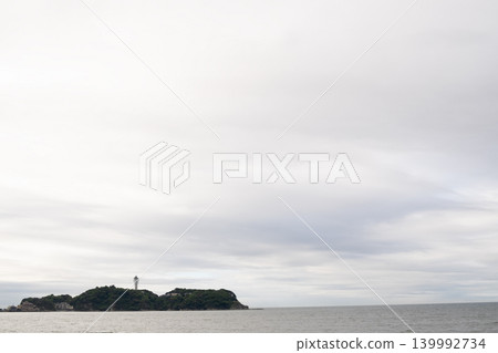 江之島和寧靜的海面,漂浮在陰雲密布的天空下。 江之島和寧靜的海面,漂浮在陰雲密布的天空下。 139992734