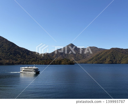 A large white sightseeing boat sails across the clear blue Lake Chuzenji. 139993787