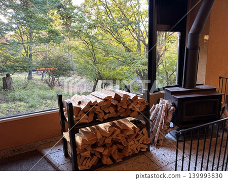 A warm wood-burning stove and firewood placed by the window. A warm wood-burning stove and firewood placed by the window. 139993830
