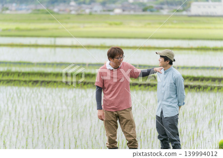 Two farmers standing on the embankment of a rice paddy. Two farmers standing on the embankment of a rice paddy. 139994012